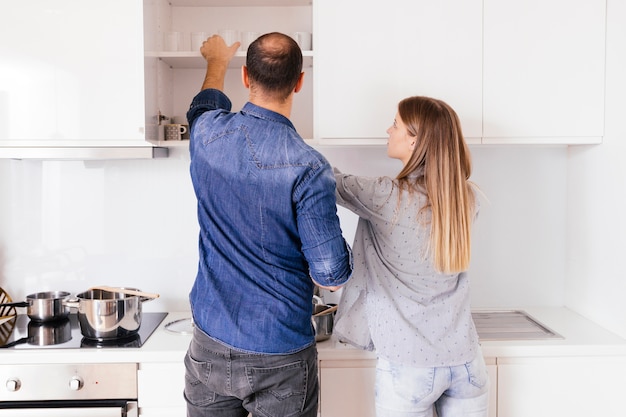 Rear view of a young couple taking glasses from the shelf