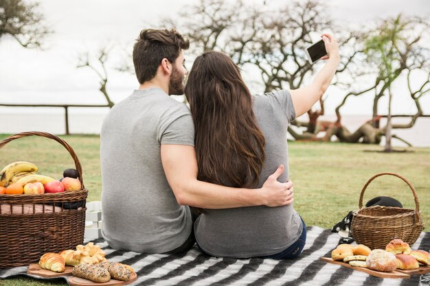 Rear view of young couple taking self portrait on cell phone in the park