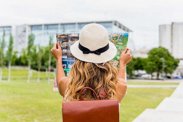 Вид сзади молодой женщины турист, носить шляпу, чтение карты в парке