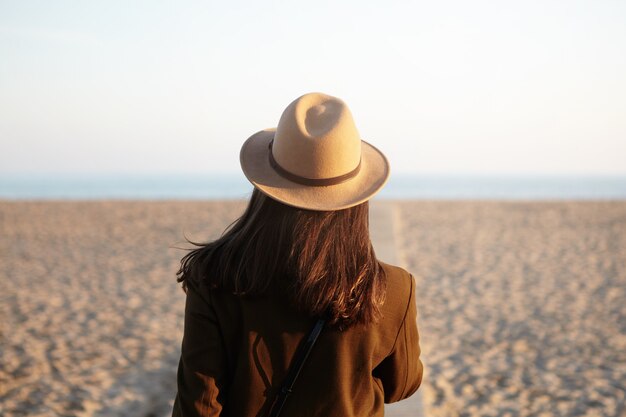 海岸線を歩いてスタイリッシュな暖かい服を着た緩い髪の若い女性の後姿