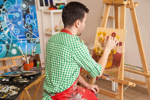 彼のスタジオで花の絵に取り組んでいる若い男性アーティストの背面図