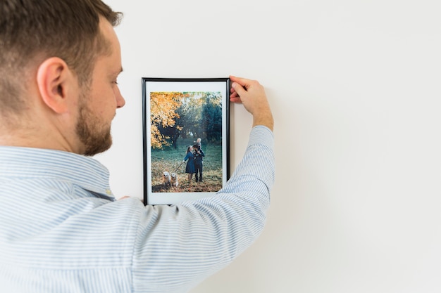 Free photo rear view of a young man holding his family picture frame on white wall