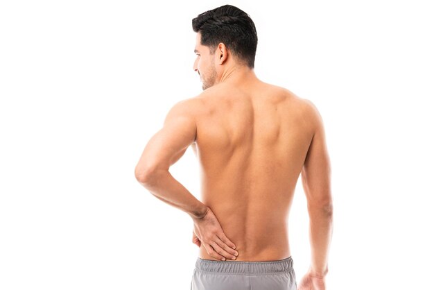 Вид сзади на молодого человека, страдающего от болей в спине на простом фоне