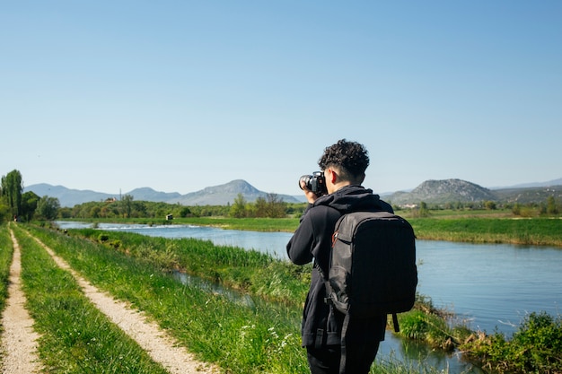 Rear view of young photographer taking photo of flowing river