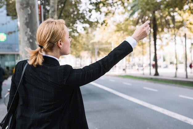 Rear view of a young woman hailing rideshare taxi car on road