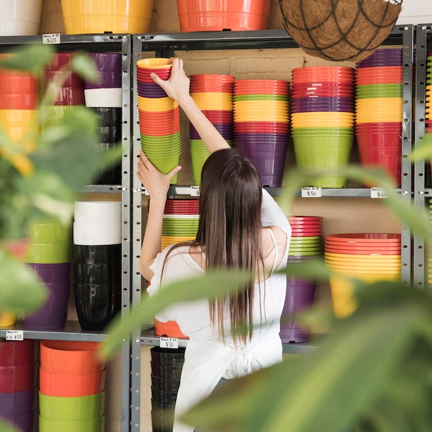 Rear view of a young woman placing colorful flowering plants in shelf