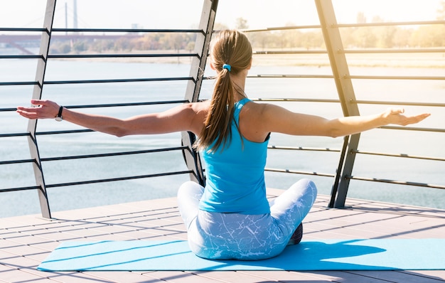 Rear view of young woman sitting on exercise mat stretching her hand sitting on bridge