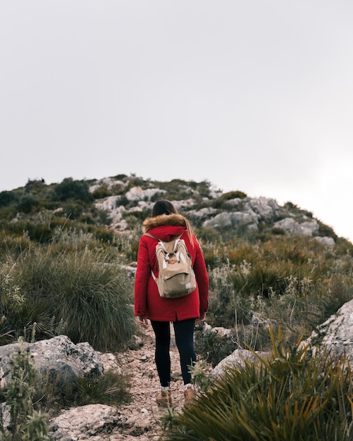 Rear view of young woman walking on mountain trail with her backpack