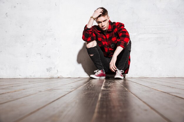 rebel man in plaid shirt posing sitting near the wall