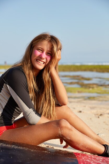 Recreation, sport and lifestyle concept. Cheerful girl likes surfing, has rest after trip