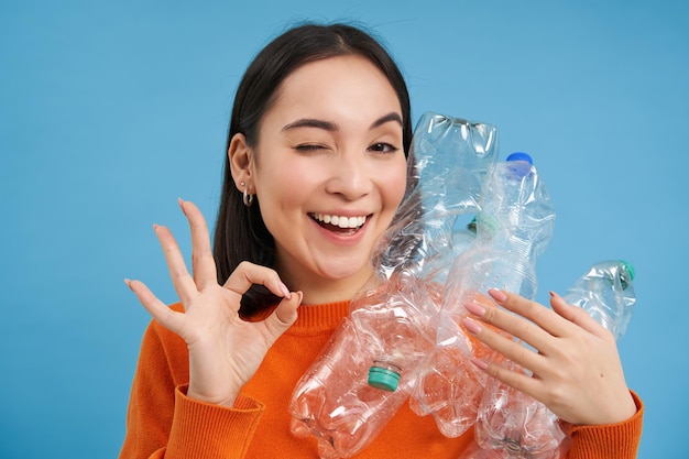 Free photo recycling is great smiling young woman holding bottles shows okay sign approves eco green lifestyle