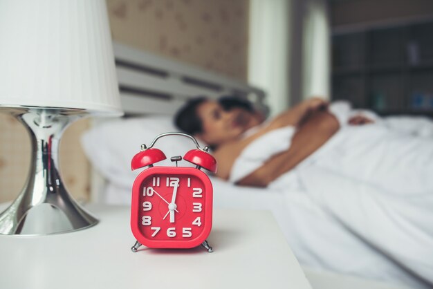 Red alarm clock with couple sleeping comfortably in bed at home