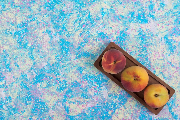 Бесплатное фото Красные и желтые персики на деревянном блюде на синем фоне в углу