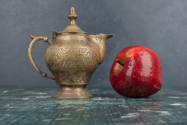 Красное яблоко и классический чайник на мраморном столе.