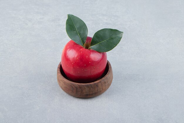 Красное яблоко с листьями в деревянной миске.