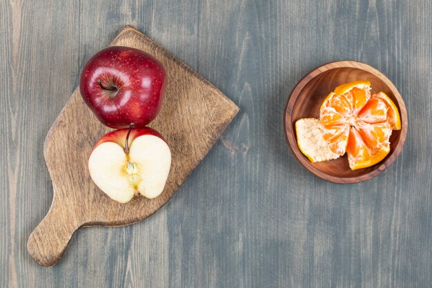 Red apple on wooden board with bowl of tangerine segments