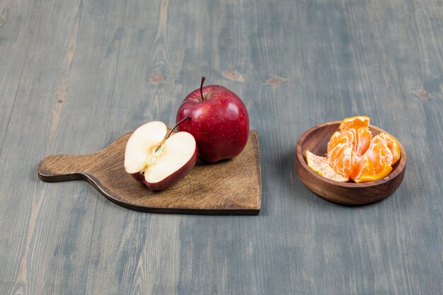 Red apple on wooden board with bowl of tangerine segments