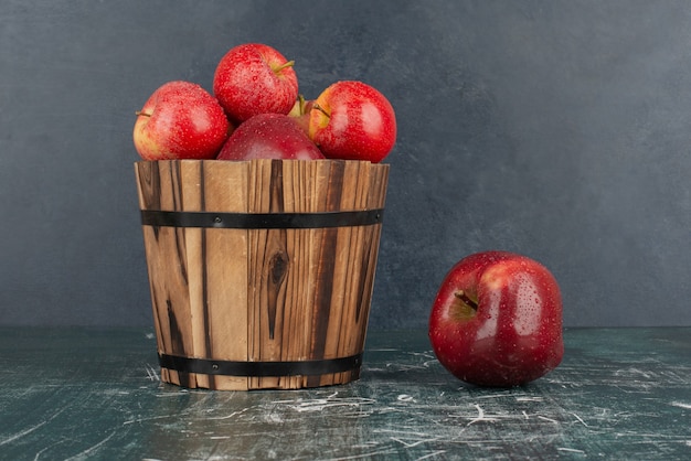 Red apples falling out of bucket on marble table.