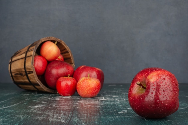 Red apples falling out of bucket on marble table.