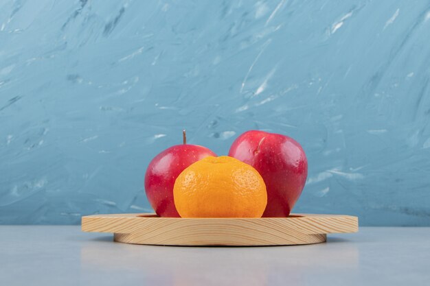 Red apples and tangerine on wooden plate