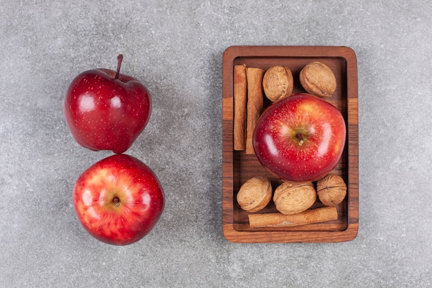 Free photo red apples, walnuts and cinnamon sticks on marble surface