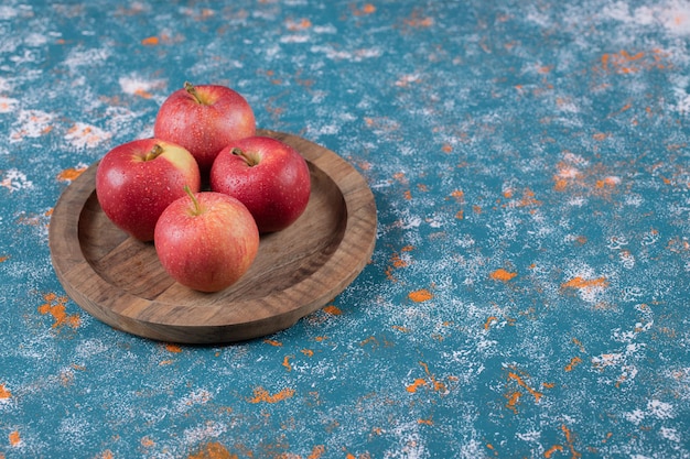Красные яблоки на деревянном блюде на синем.