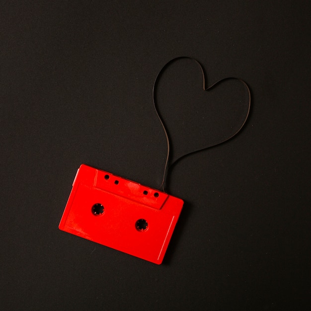 Red audio cassette with magnetic tape in shape of heart on black background