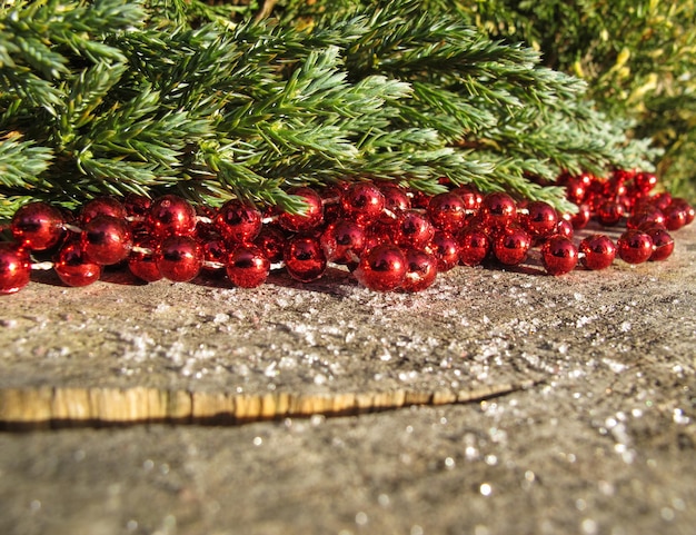 Red beads and conifer branches on a background of rustic wood with snow in sunny day space to copy