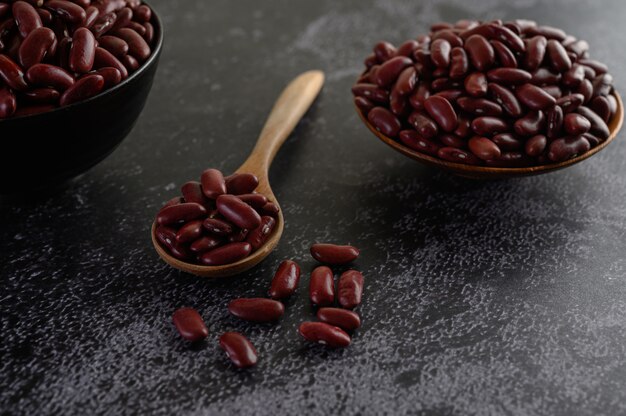 Red beans in a wooden bowl and wooden spoon on the black cement floor.