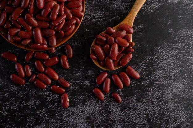 Red beans in a wooden bowl and wooden spoon on the black cement floor.