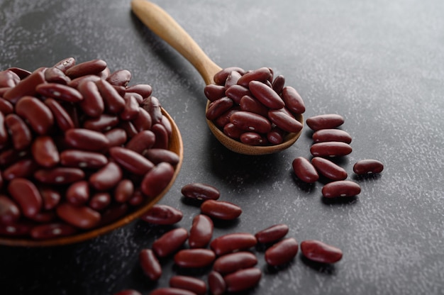 Fagioli rossi in una ciotola di legno e cucchiaio di legno sul pavimento nero del cemento.