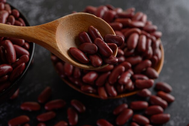 Red beans in a wooden bowl and wooden spoon on the black cement floor.