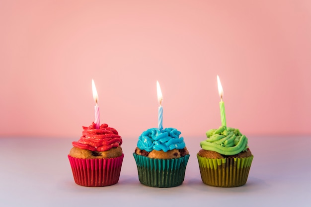 Red; blue and green cupcakes with an lighted candles against pink backdrop