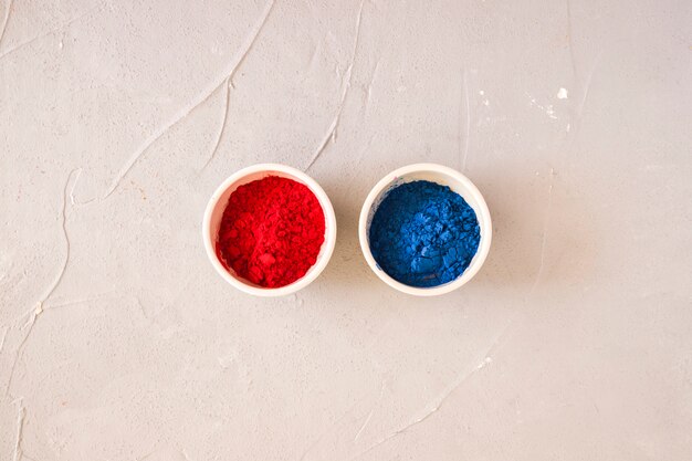 Red and blue holi colored powder in the white bowl on backdrop