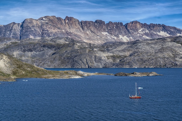 Barca rossa sul mare blu che osserva la montagna grigia sotto i cieli blu e bianchi