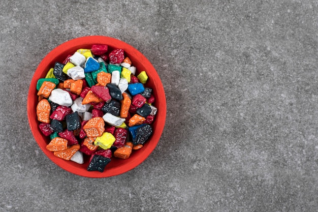 Red bowl of colorful stone candies on stone.