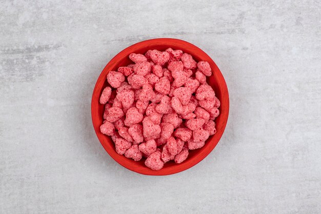 Red bowl full of pink cereals on stone table.