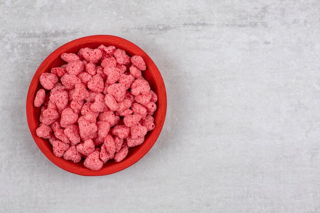 Red bowl full of pink cereals on stone table.