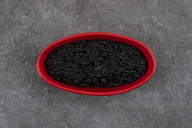 Red bowl full with black caviar on grey table.