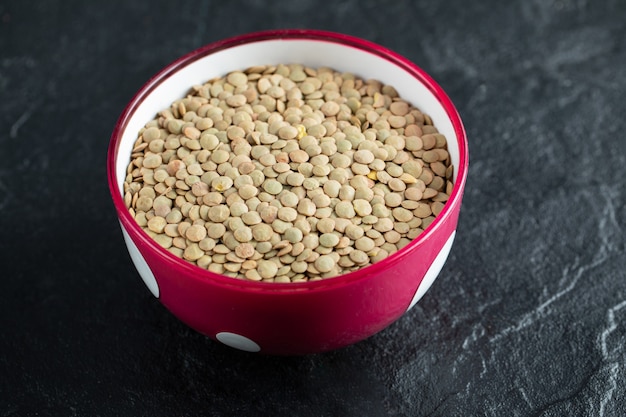 Una ciotola rossa con le lenticchie crude marroni secche sul nero.