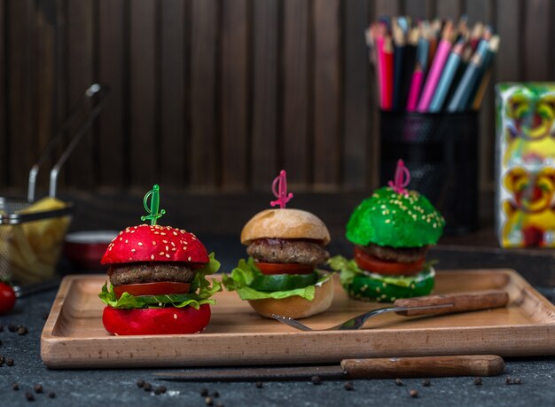 Red brown and green bread bun burgers in a tray.