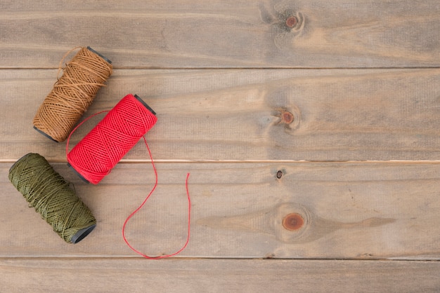 Red; brown and green yarn spool on wooden table