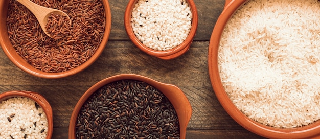 Red; brown and white rice in bowls on wooden background
