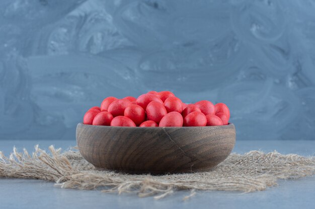 Red candies in the cup on the trivet, on the marble table. 