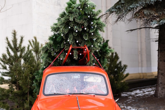 雪景色の中でクリスマスツリーを運ぶ赤い車。テキスト用のスペース。