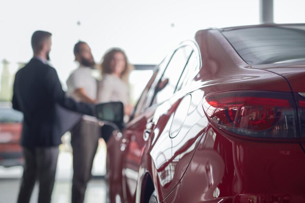 Red car close up clients of car dealership behind