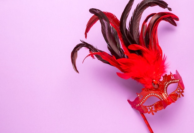 Red carnival mask with feathers on pink background with copy space