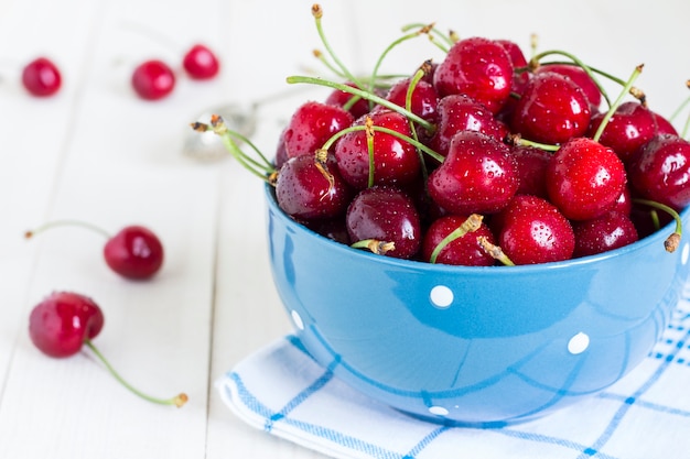 Red cherries in bowl on white wood on blue towel