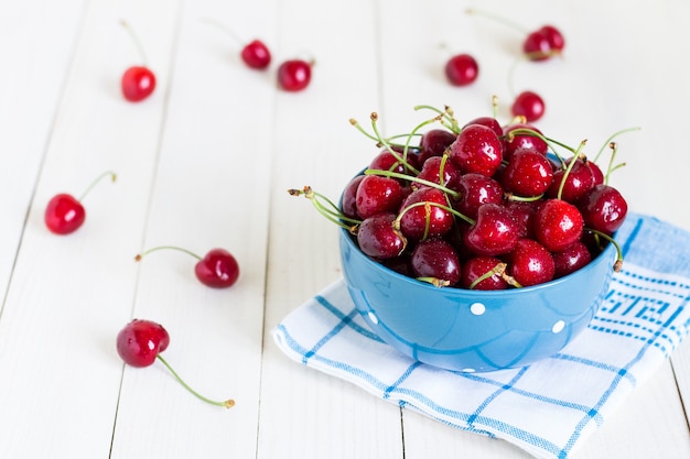 Red cherries in bowl on white wood on blue towel