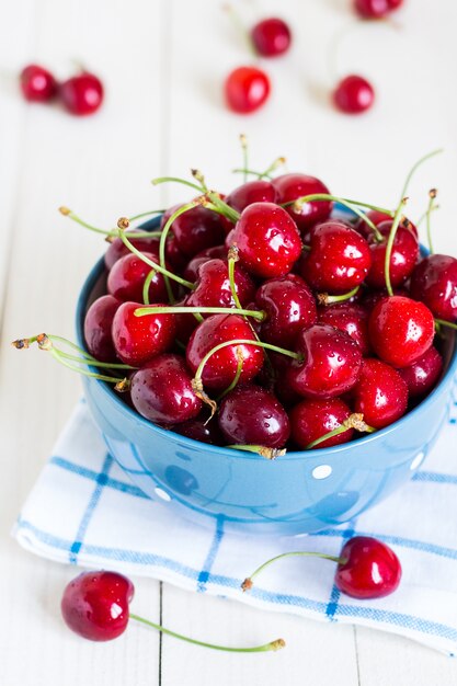 Red cherries in bowl on white wood on blue towel